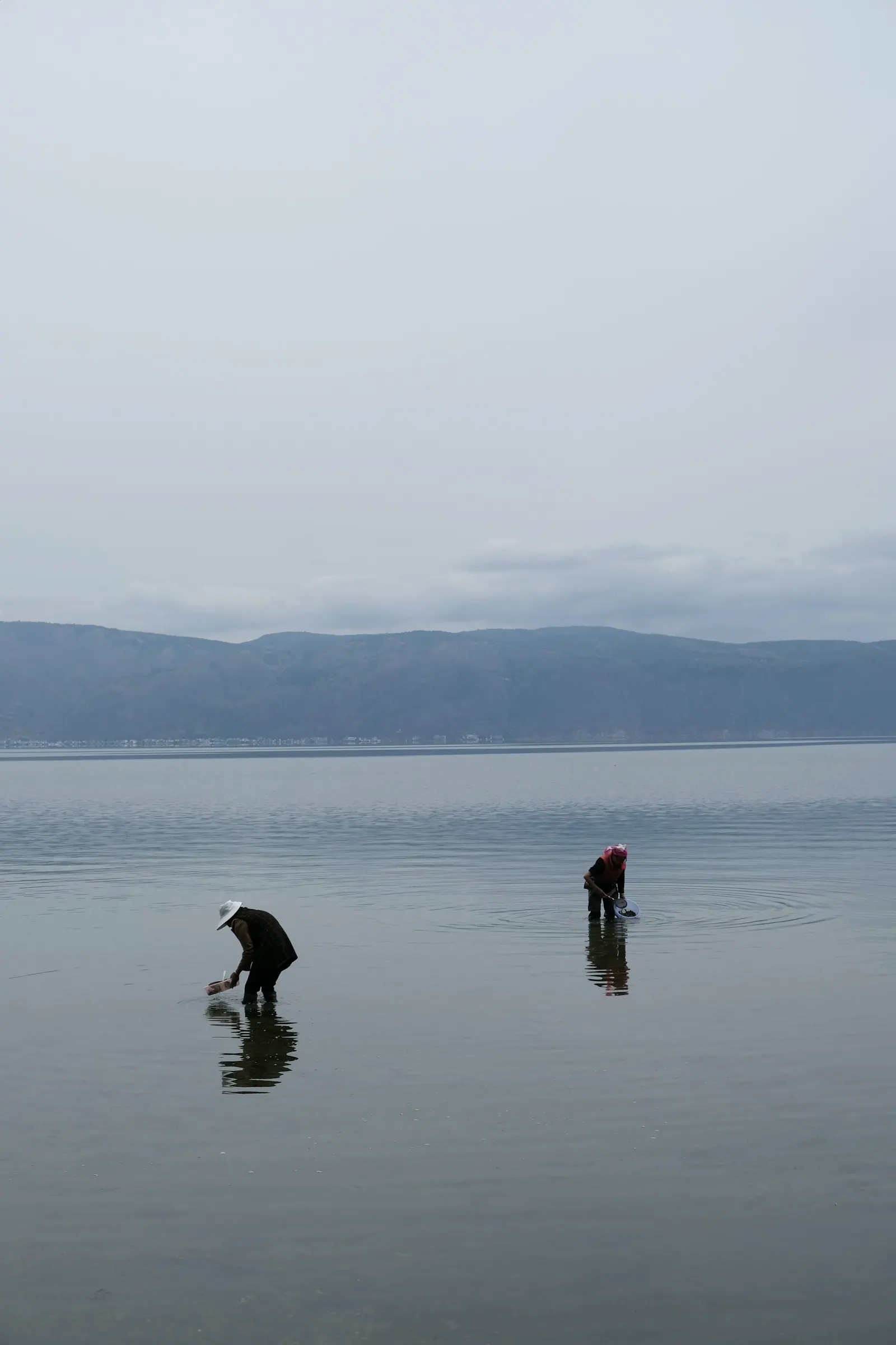 Two figures standing in shallow water on the lake at dawn