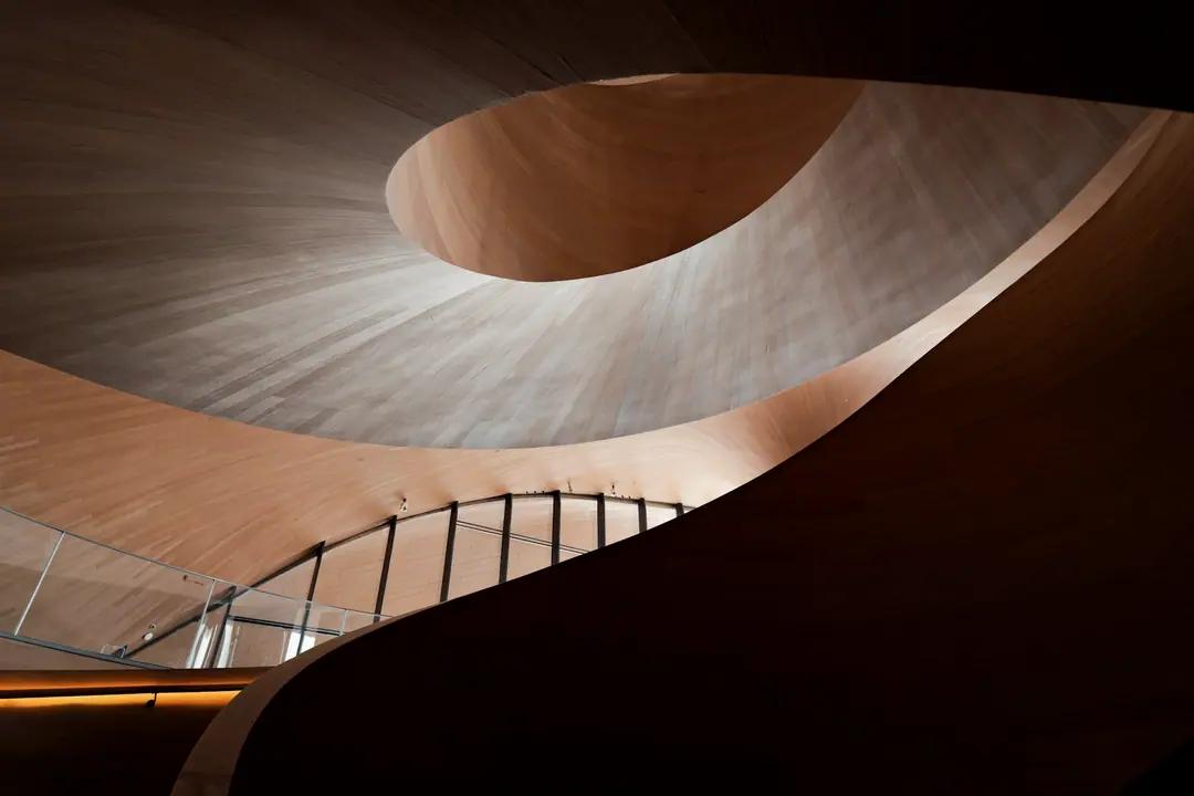 A beam of light falling across a wooden spiral staircase from the side