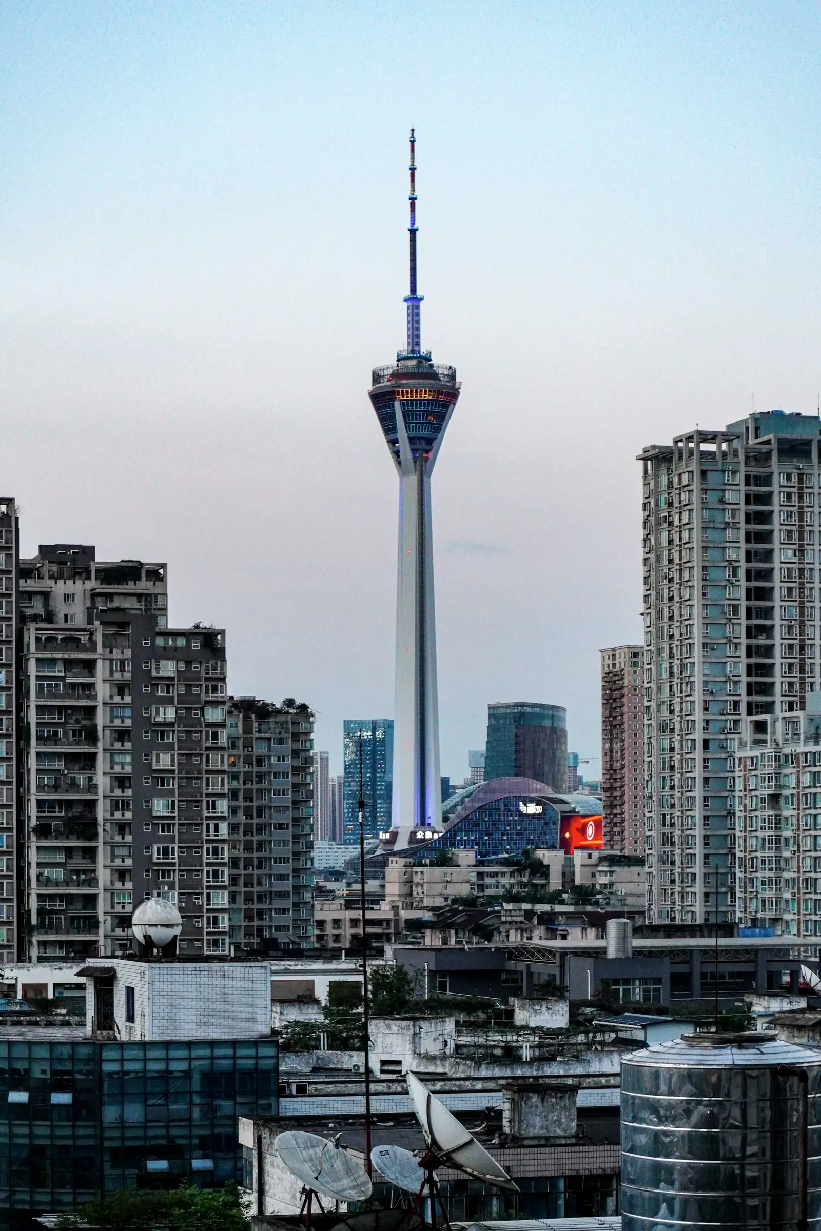 Under a pale grey sky, a TV tower rising from a sea of apartment blocks