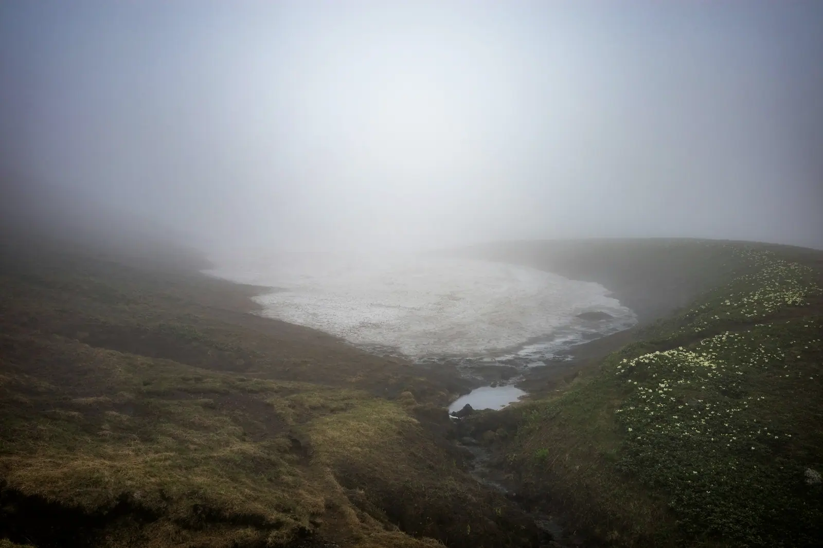 A lake and grass slope faintly visible through the mist