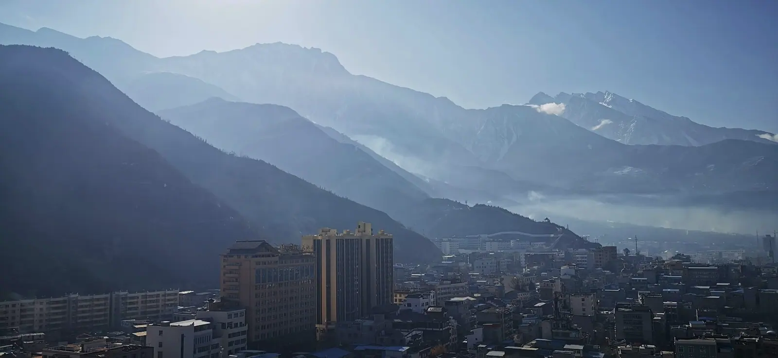 A mountain town in thin mist, buildings crowded at the foot of the hills, ridges fading layer by layer behind