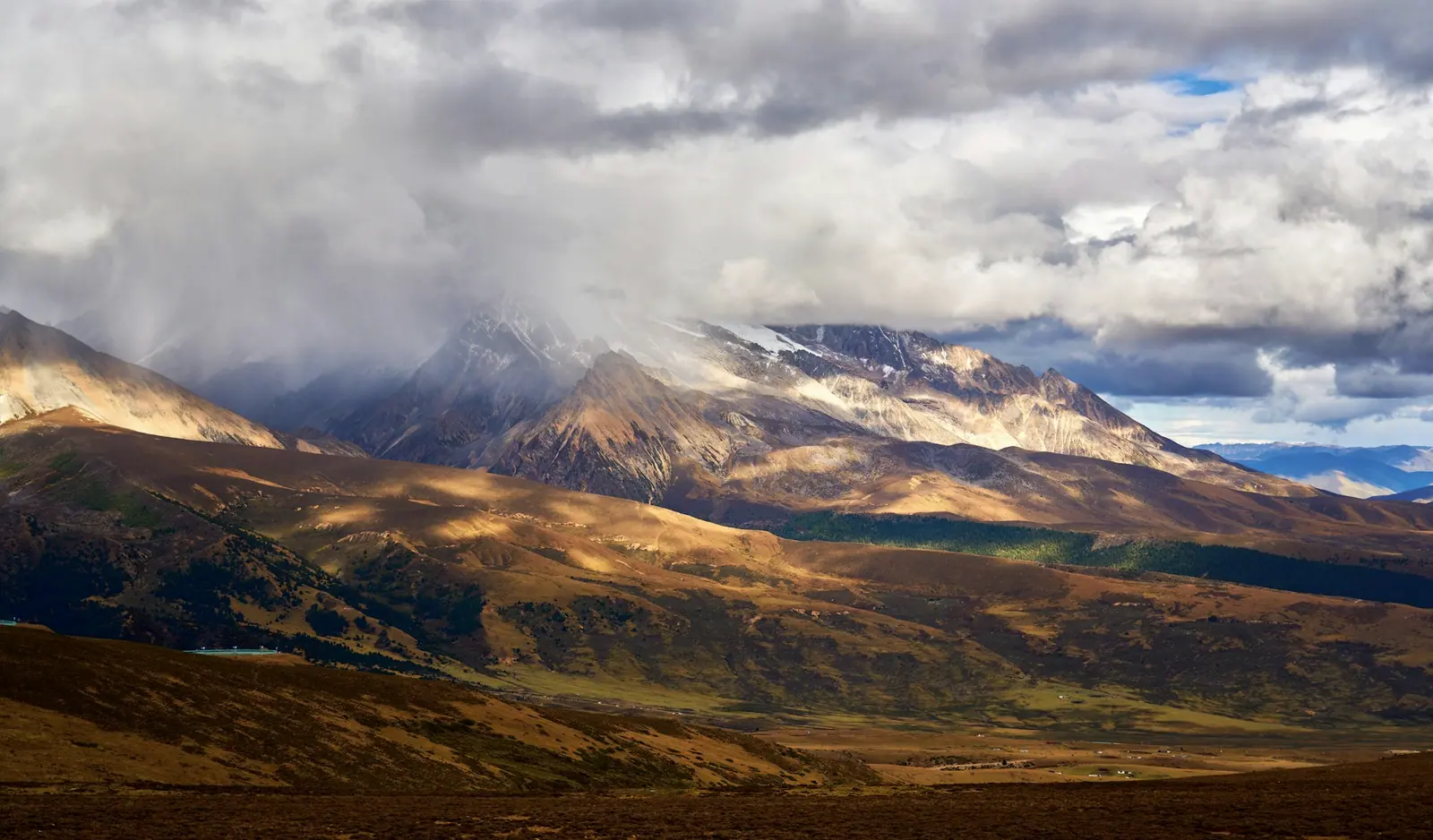 Cloud pressing down on the summit, a shaft of light falling on a golden grass slope