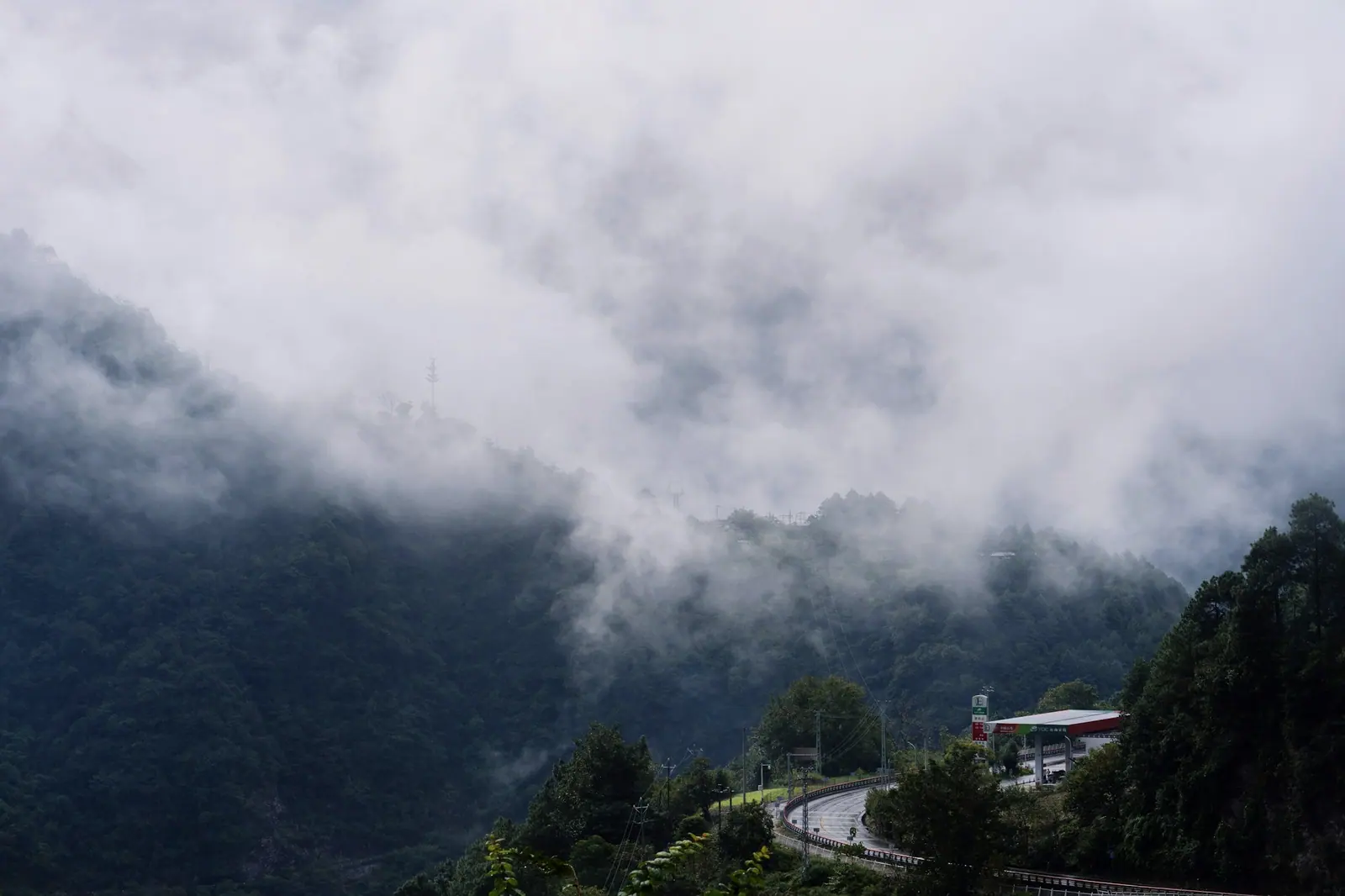 Thick fog climbing the hillside, a road winding up into the cloud
