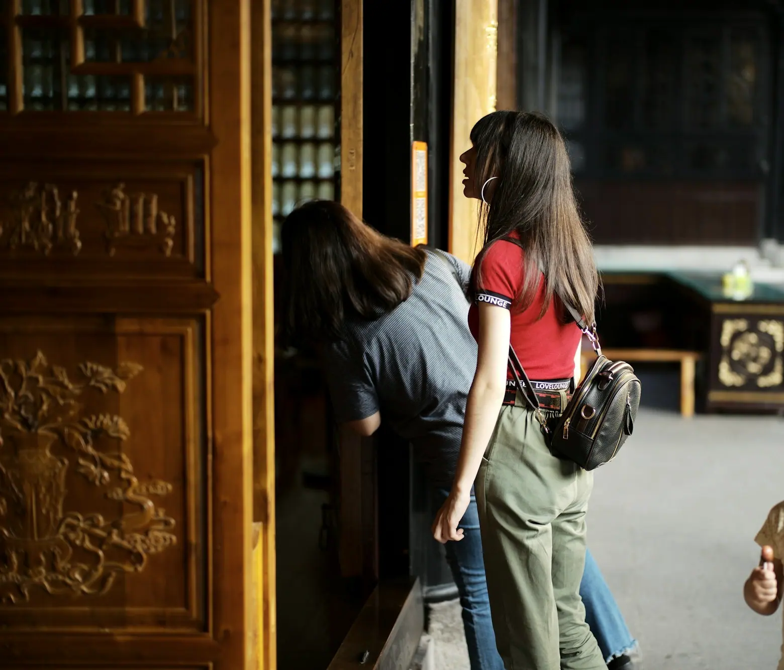 A few people leaning in to peer through the carved doors and windows of an old house, a child standing beside them