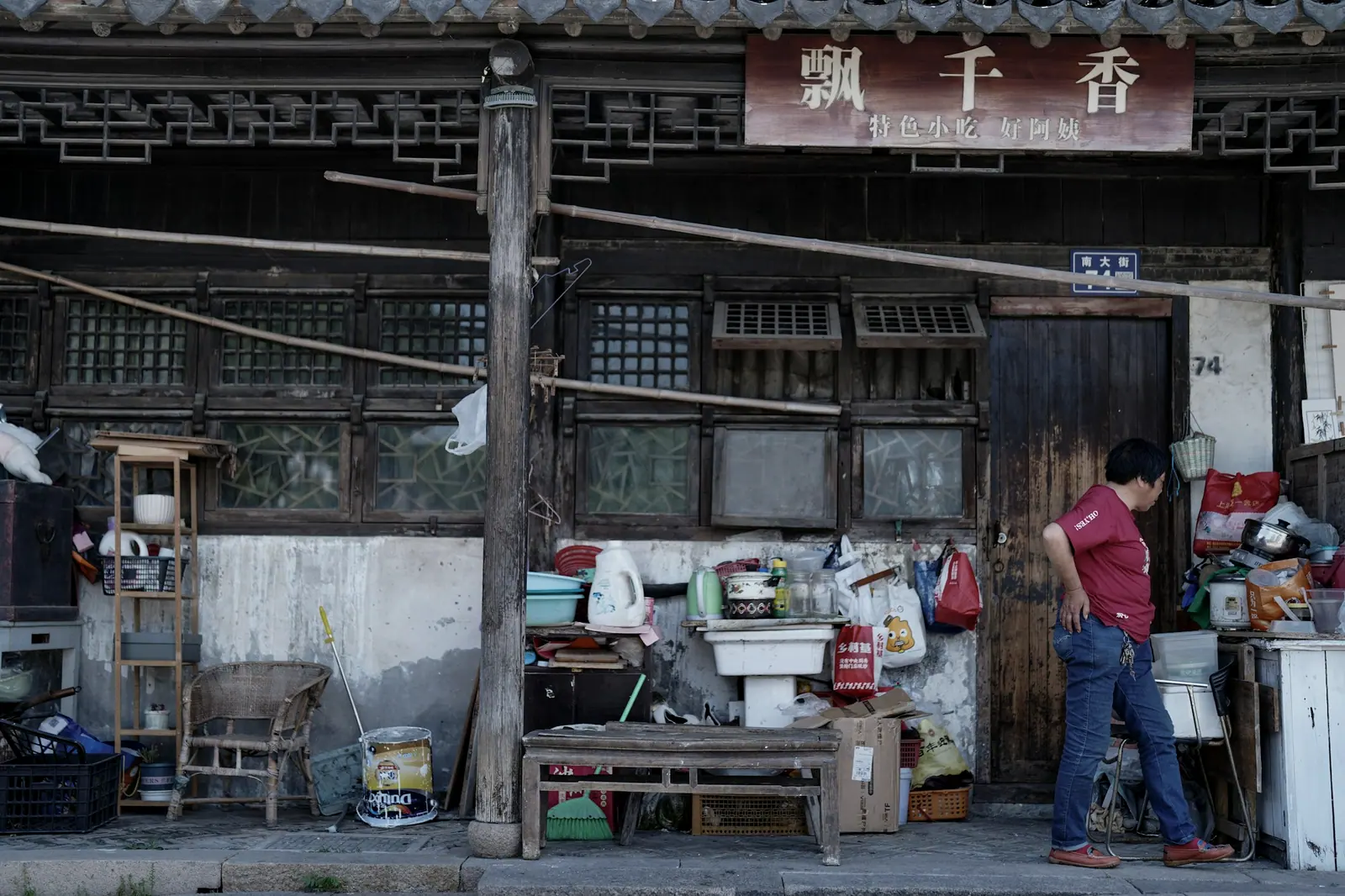 A person standing in the doorway of an old shop crowded with odds and ends, a hand-painted sign above