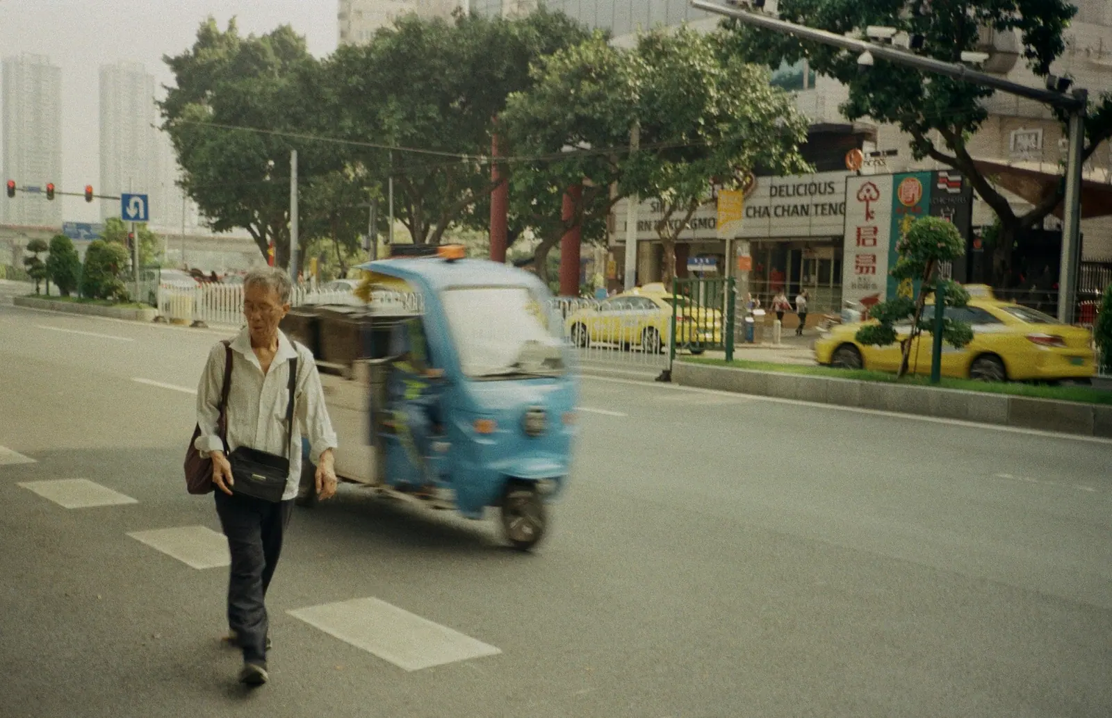 An elderly man crossing at a junction, a blue tricycle behind him