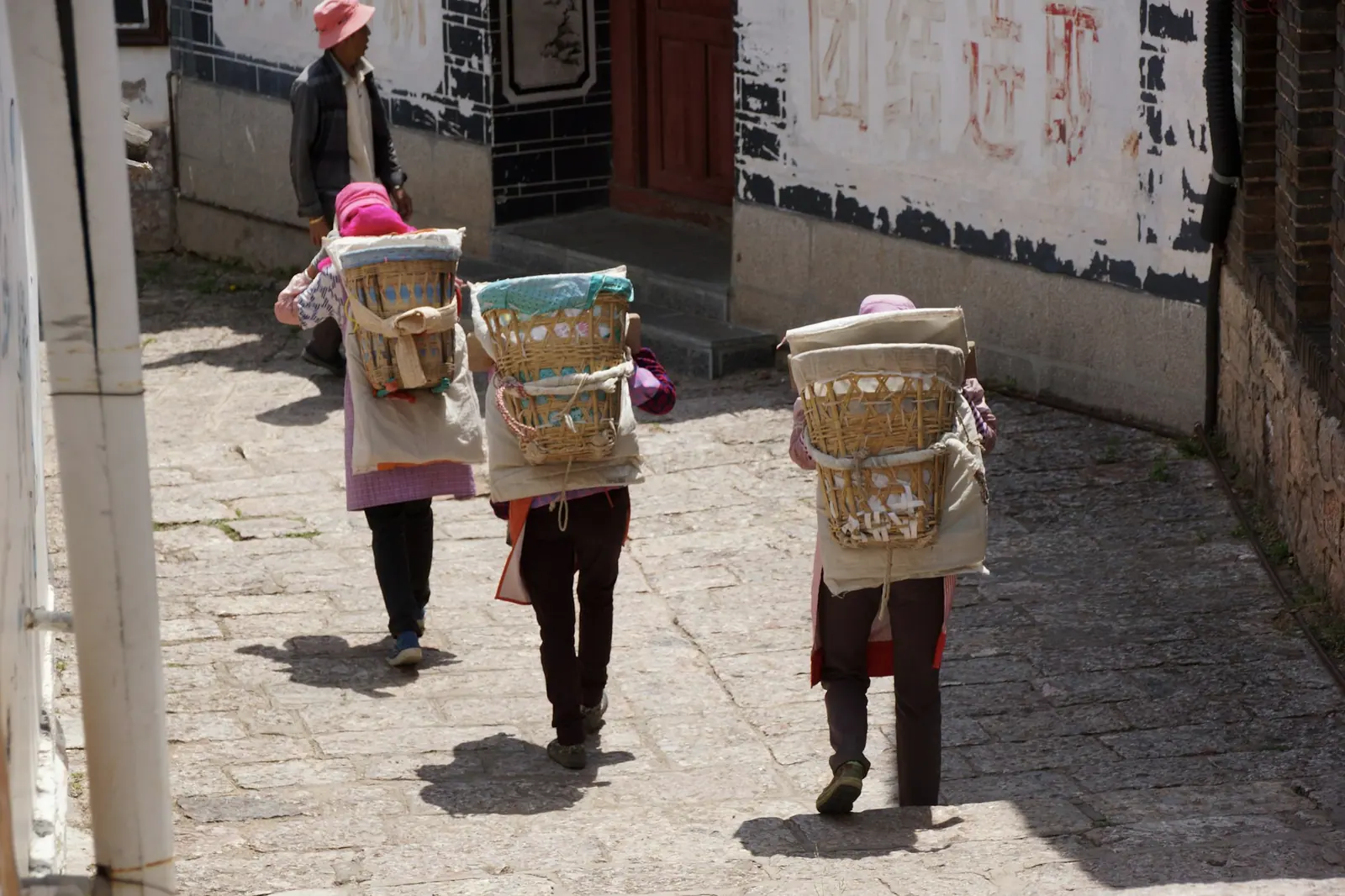 Three people with bamboo baskets on their backs walking along a flagstone road