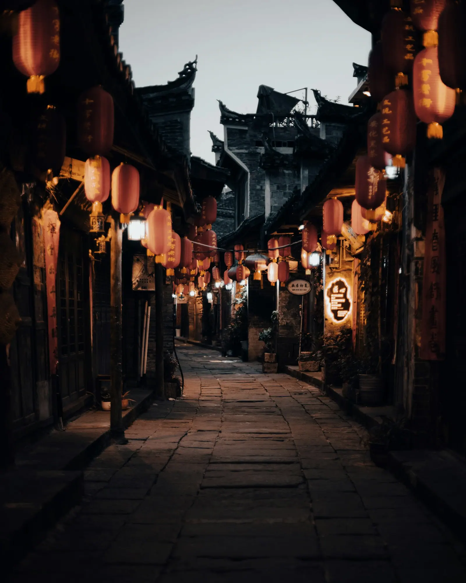 An old street strung with red lanterns, a few people walking along it