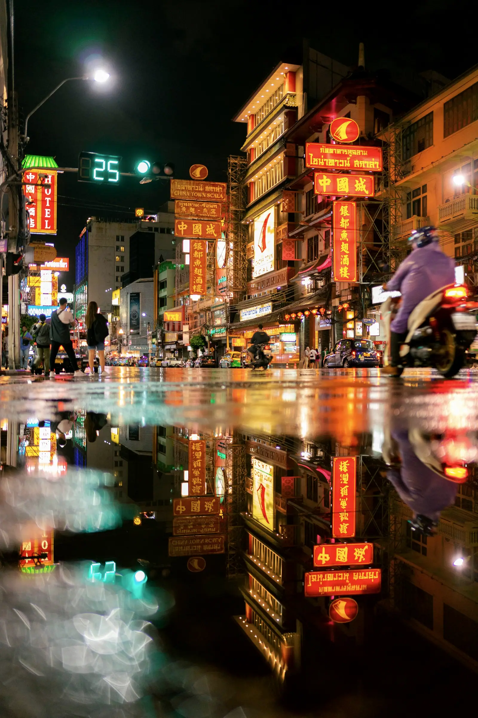 A man on a motorbike rides through neon reflected on the wet road