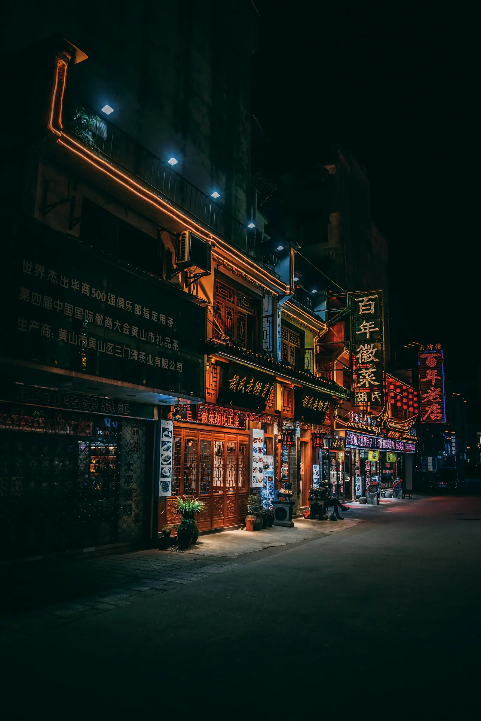 An old-style shop still lit at night, its red sign spilling onto the pavement