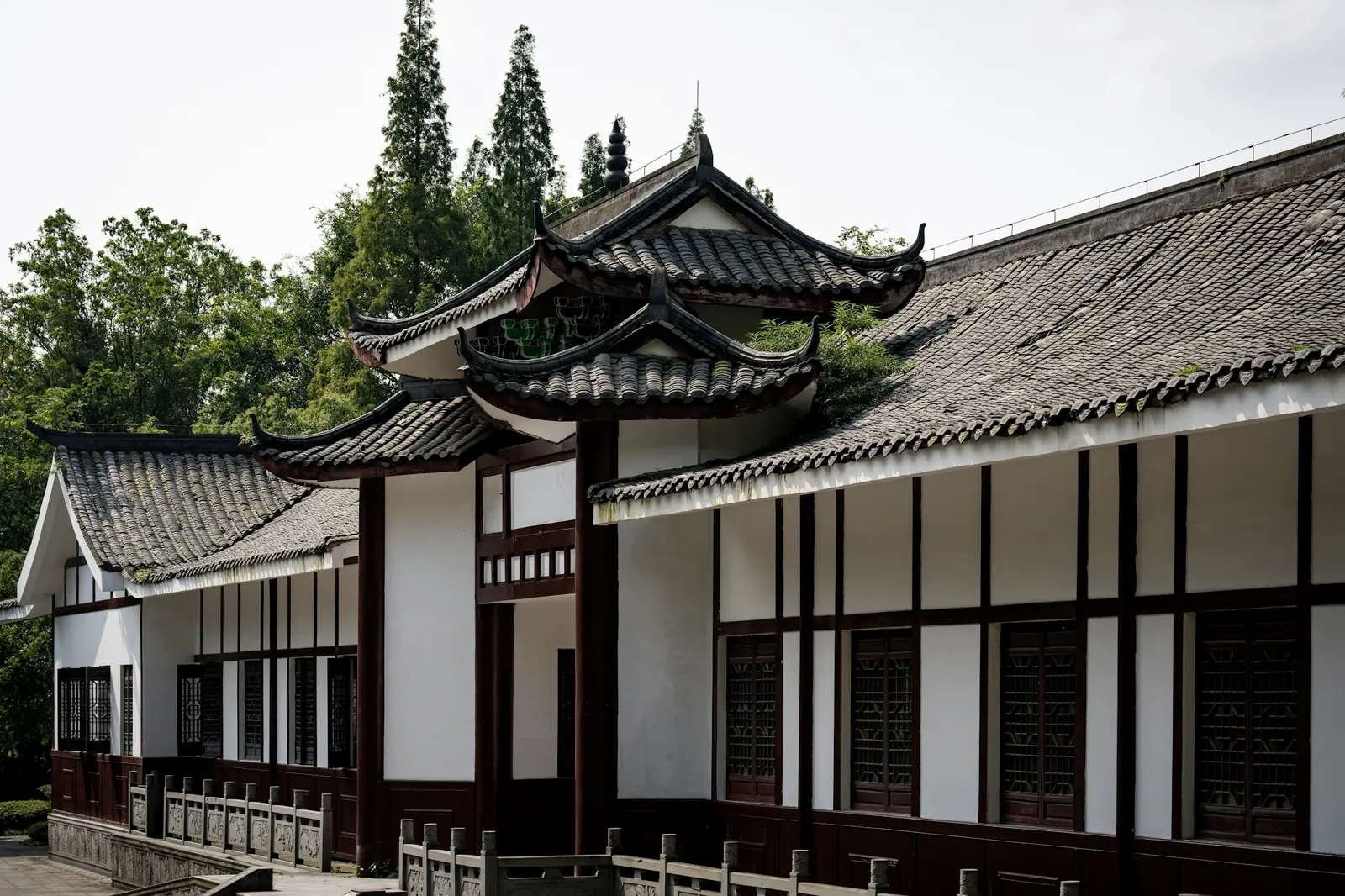 An old house on a hillside in western Sichuan, white walls and dark timber, eaves stacked in layers