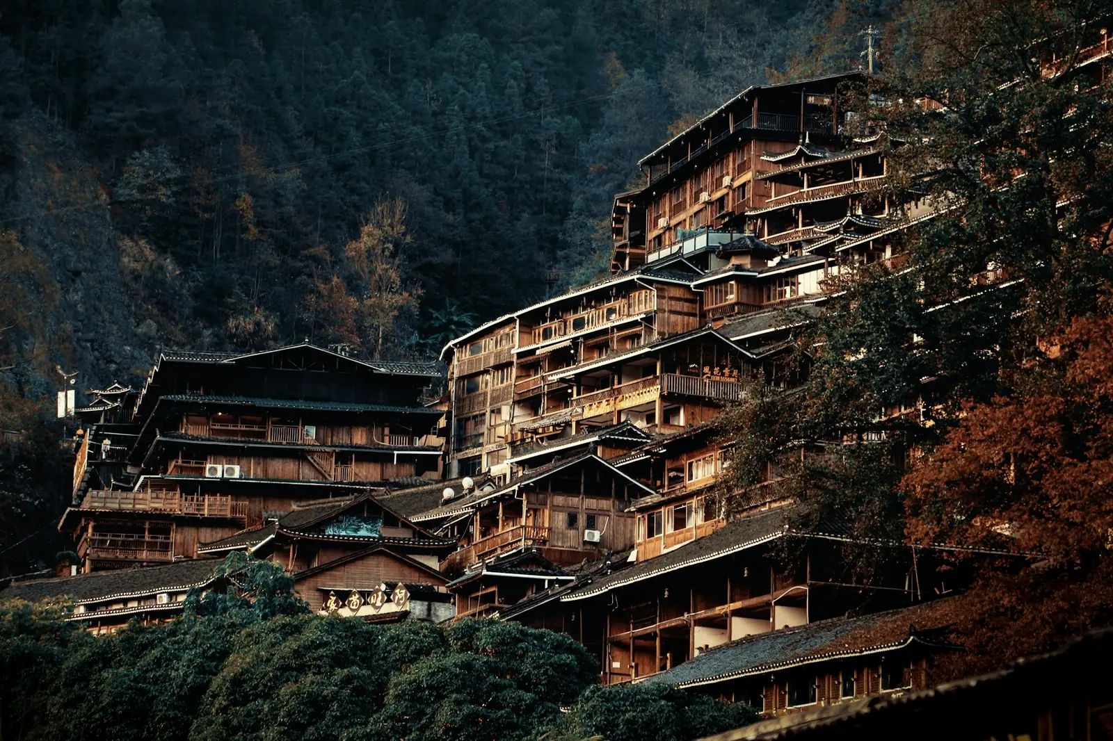 Timber houses stacked up a hillside, warm yellow light in the windows