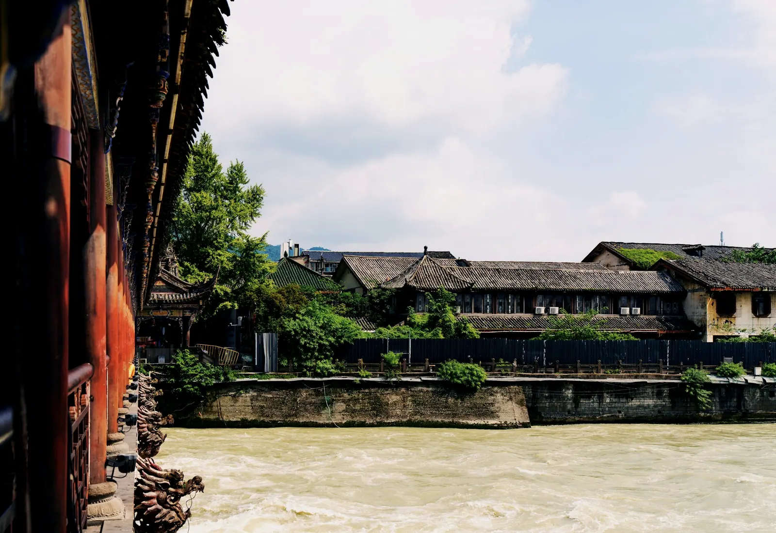 A river spilling over a gravel bank, a row of old houses on the far side, stone beasts under the eaves leaning out toward the water