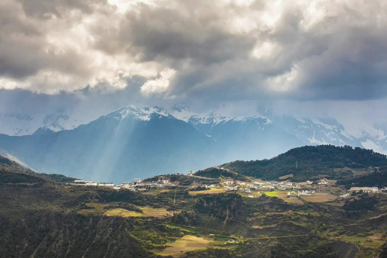 Cloud pressing down on distant snow peaks, light leaking through the gaps