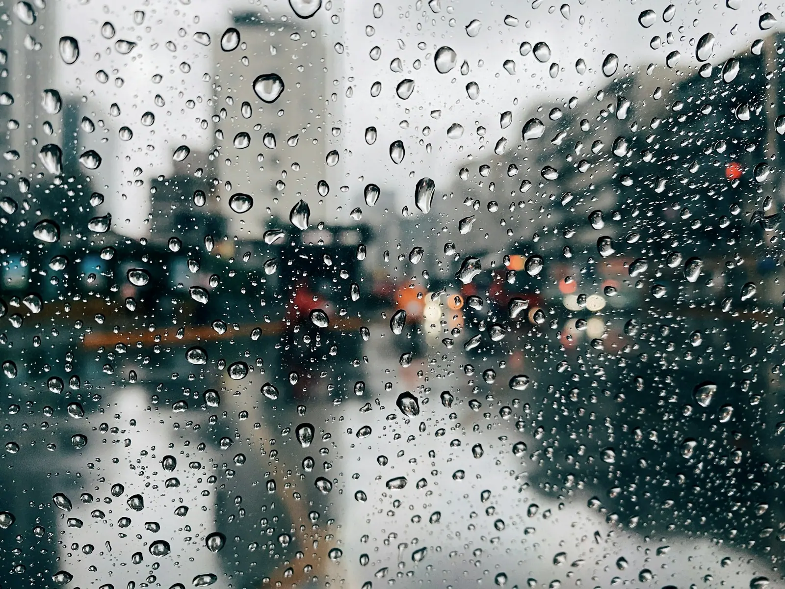 A rain-beaded car window, street lamps and headlights smeared into one blur of light