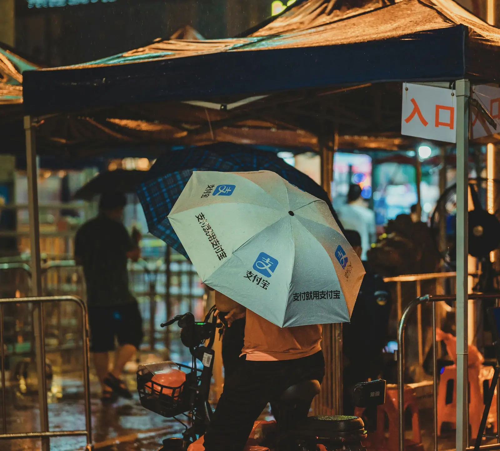 A person under an umbrella in the light of a street stall