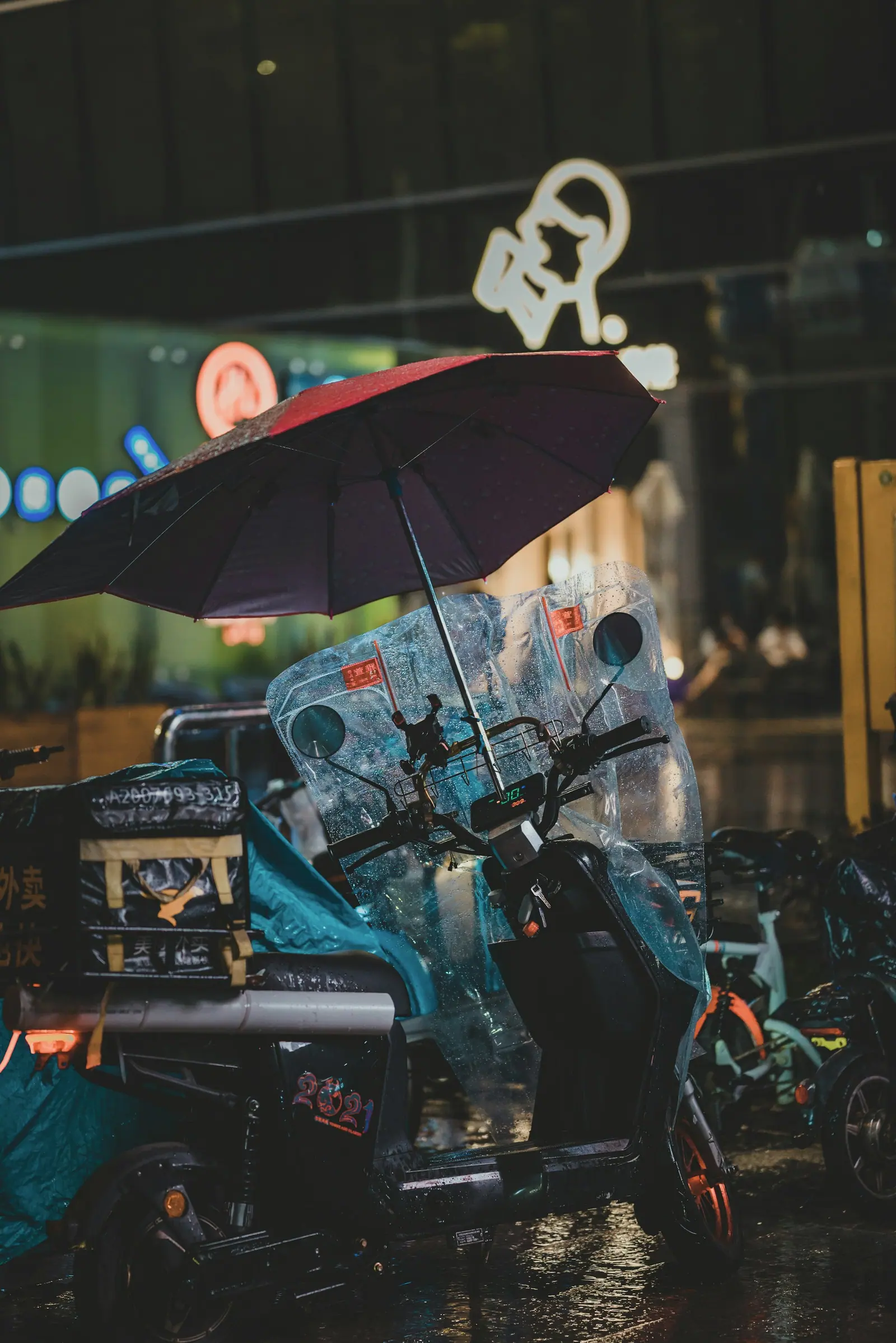 An electric scooter parked in the rain with an umbrella propped over it