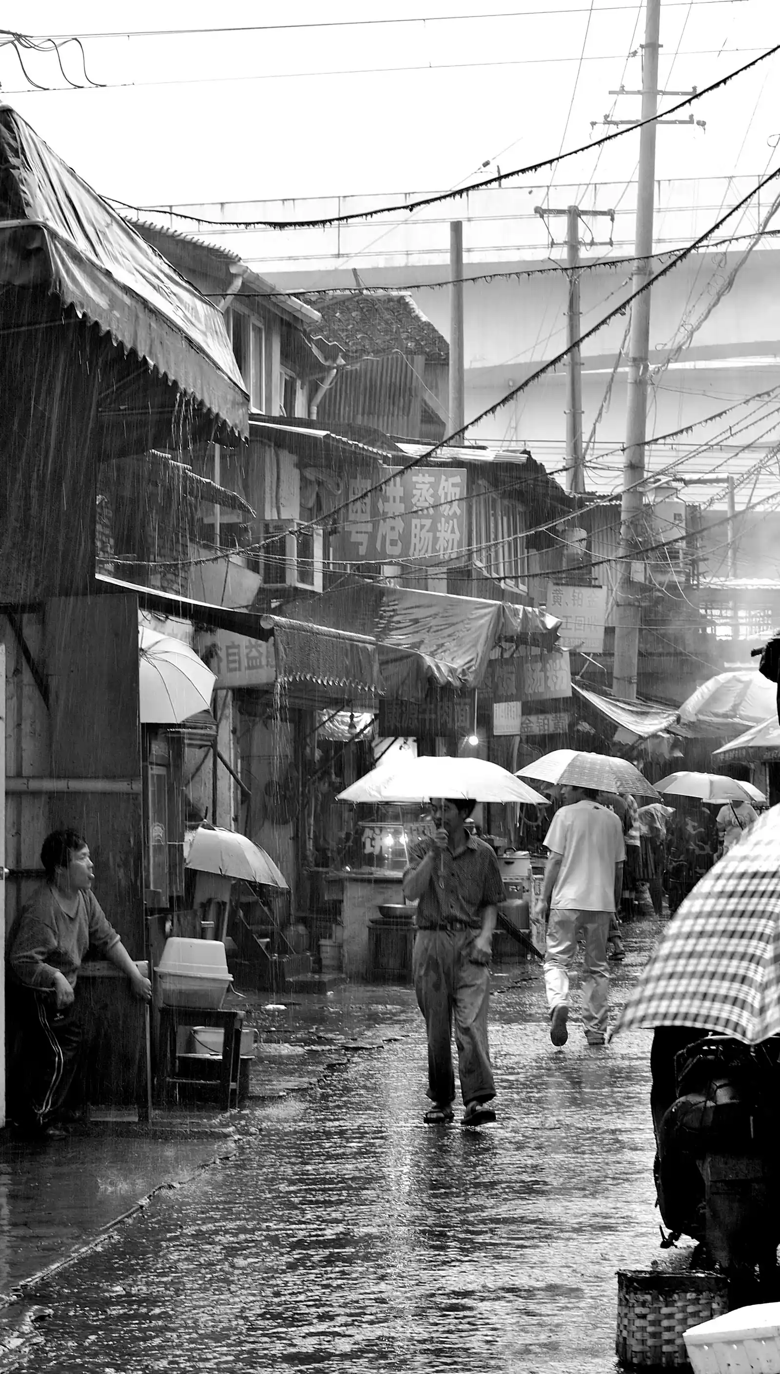 A black-and-white photo of a man with an umbrella walking down a wet street