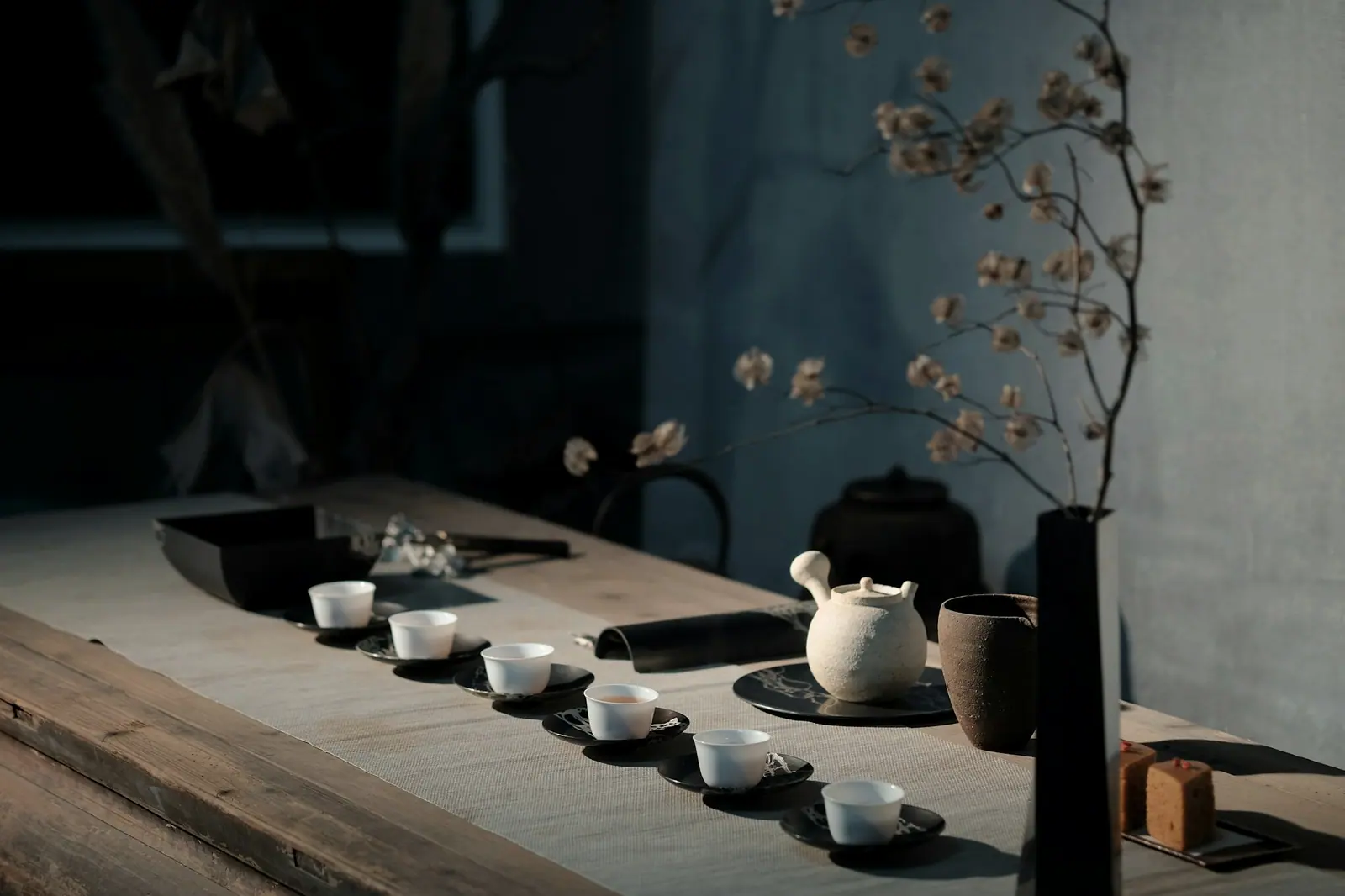 Small white porcelain cups and a teapot laid out on a wooden table