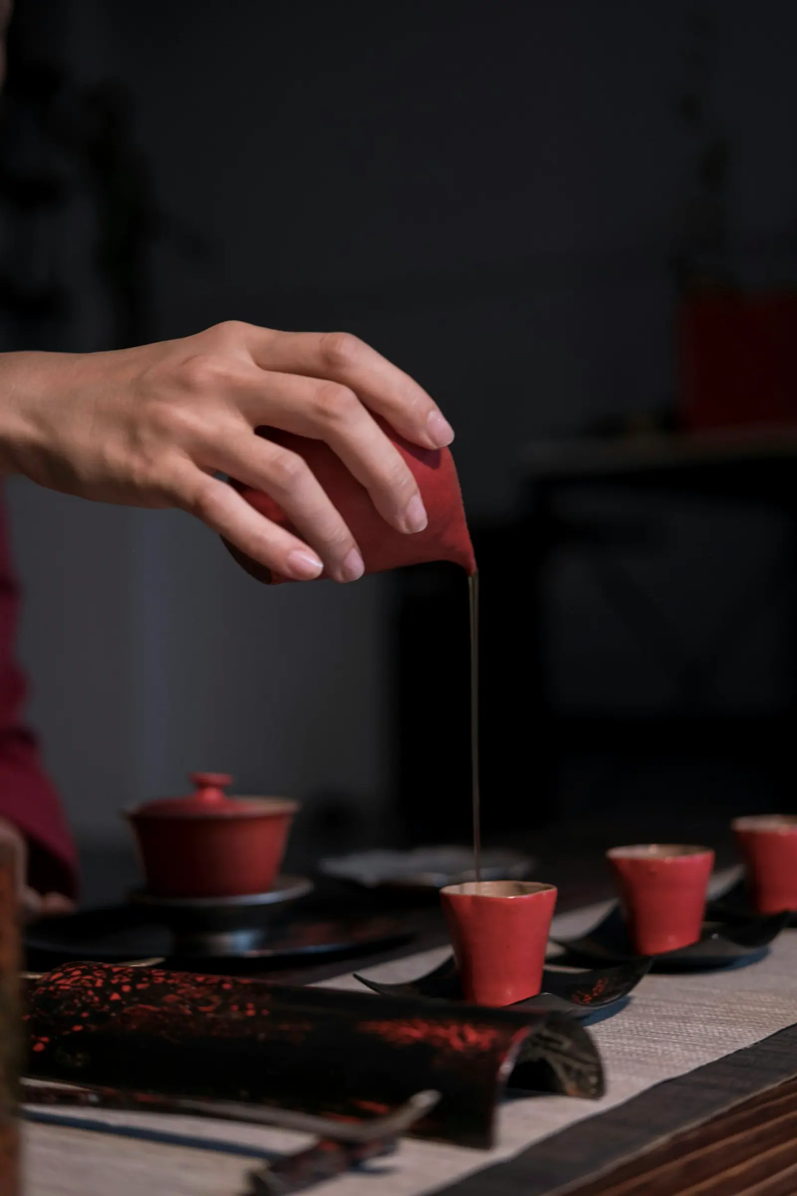 A hand pouring tea into a small red cup