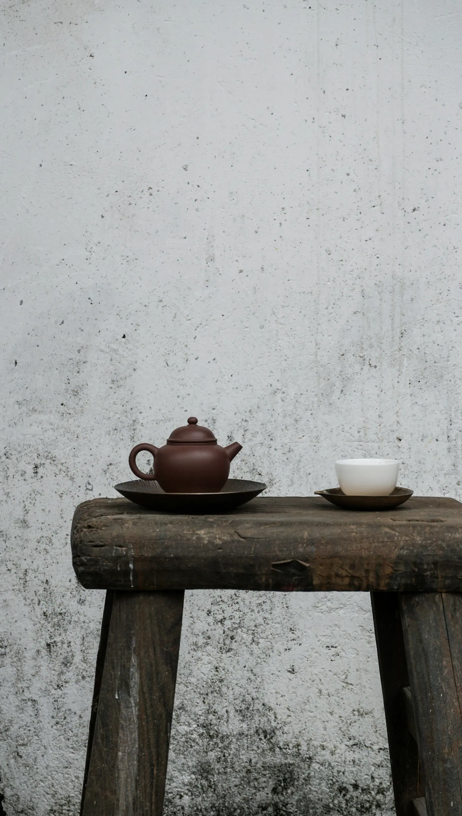 A teapot on a small stool beside a pale grey wall